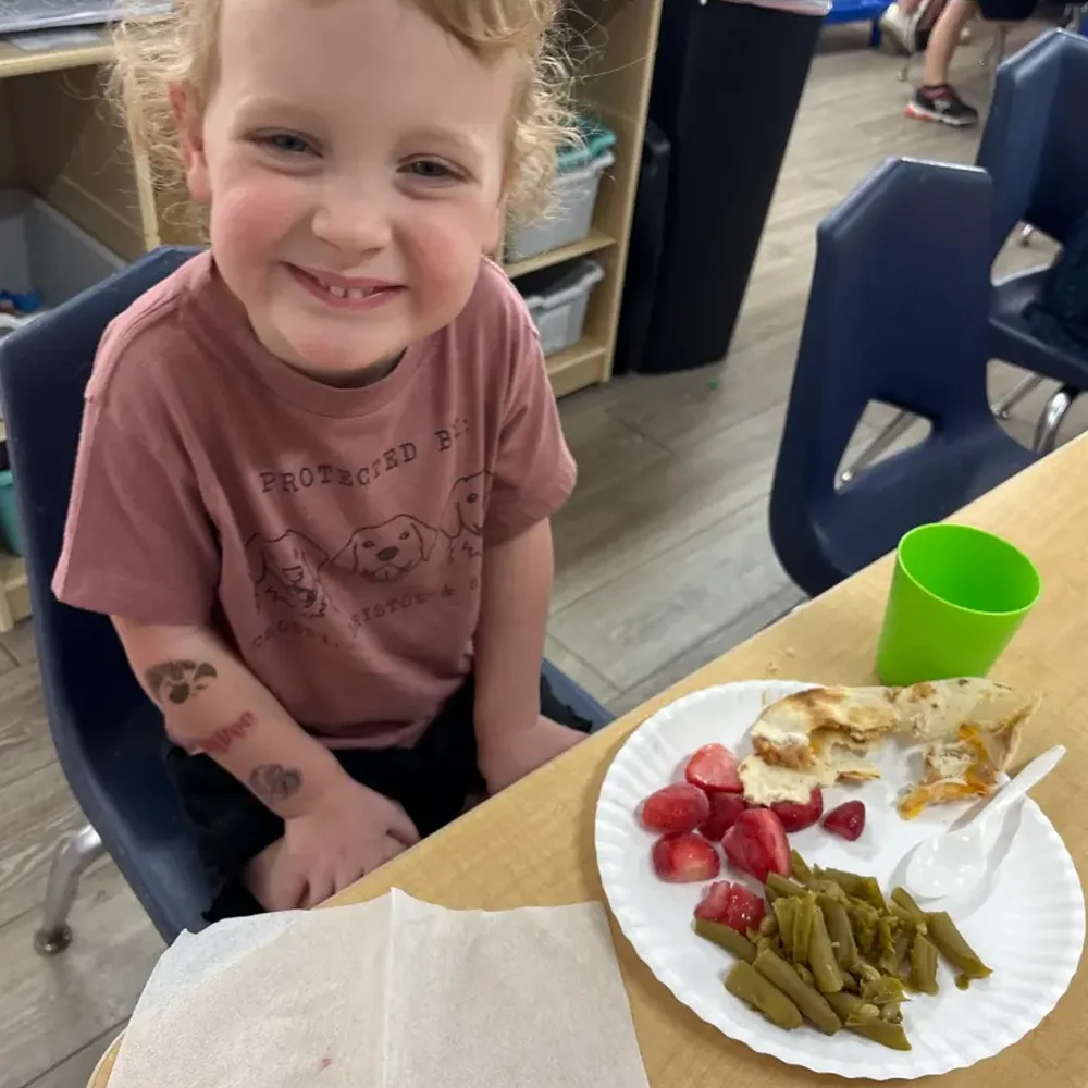 Smiling preschooler at a lunch table with a scratch made meal in the Hummingbirds preschool room at The Nest