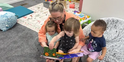 A teacher reading a picture book to three toddlers in the Flamingos transition room at The Nest